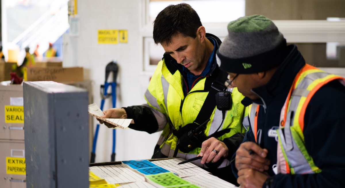 Two Lineage employees in high vis vests working over paper in a warehouse