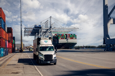 A Lineage Logistics truck at a bustling port, surrounded by shipping containers and cranes, showcasing seamless integration of cold storage and global logistics.