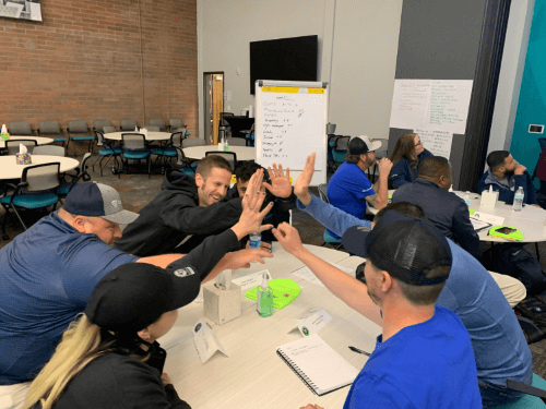 Lineage EDGE Program participants engaging in a lively team-building activity indoors, sharing high-fives and enthusiasm around a collaborative workspace.