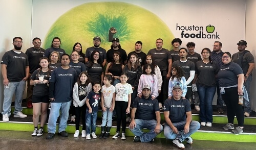 A group of dedicated Lineage volunteers, including families and children, pose together at the Houston Food Bank, wearing matching 'Volunteer' shirts, united in their mission to give back to the community.