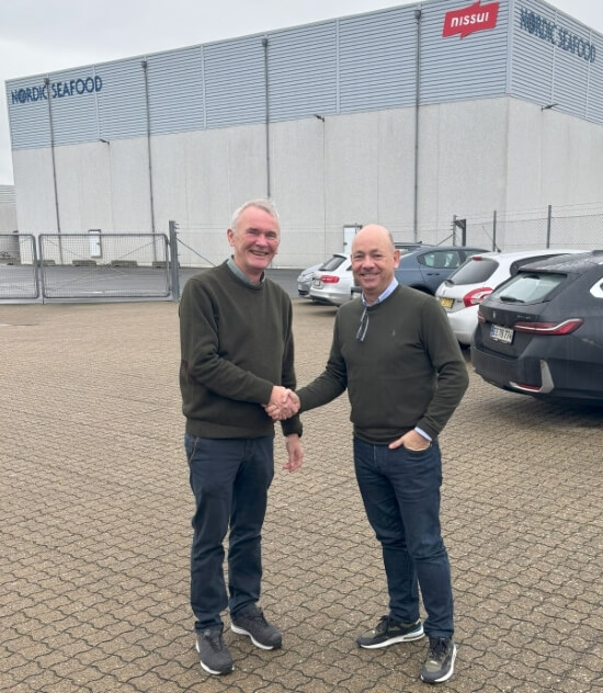 wo men shaking hands outside a Lineage/Nordic Seafood facility, marked with the Nissui logo, symbolizing their long-standing Lineage/Nordic Seafood partnership in seafood distribution.