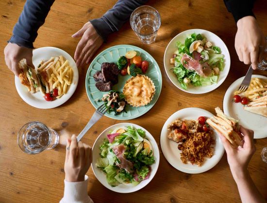 A group of people reach for food arranged on plates on a wooden table