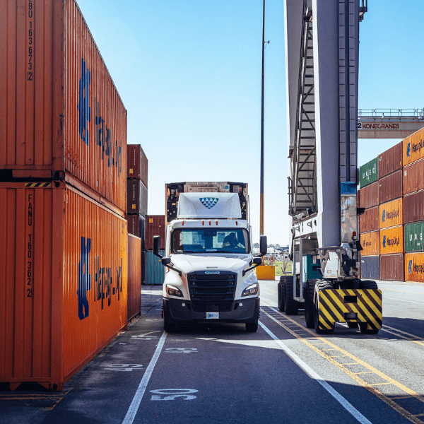 Lineage truck positioned between stacked cargo containers and a crane at a port, illustrating port-centric location, integrated transportation solutions and drayage services.