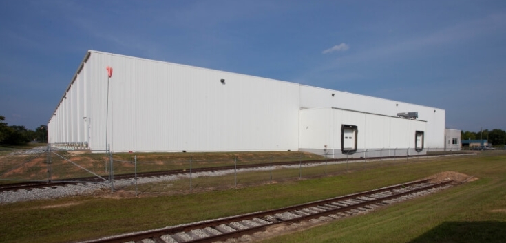 Exterior side view of Lineage’s Macon cold storage facility in Atlanta, Georgia, featuring a white warehouse, adjacent rail tracks, and a grassy foreground.