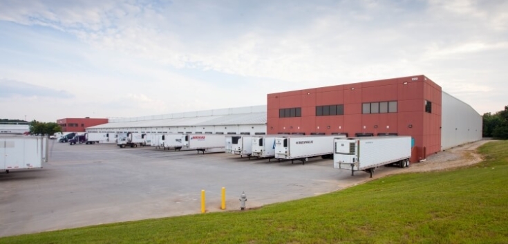 Side view of Lineage’s McDonough - 200 King Mill cold storage facility, showcasing docked refrigerated trailers, a red-brick structure, and open loading areas.