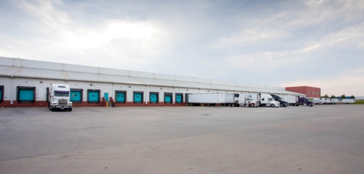 Dockside view of Lineage’s McDonough - 200 King Mill cold storage facility, featuring multiple loading bays, semi-trailers, and a spacious concrete yard.