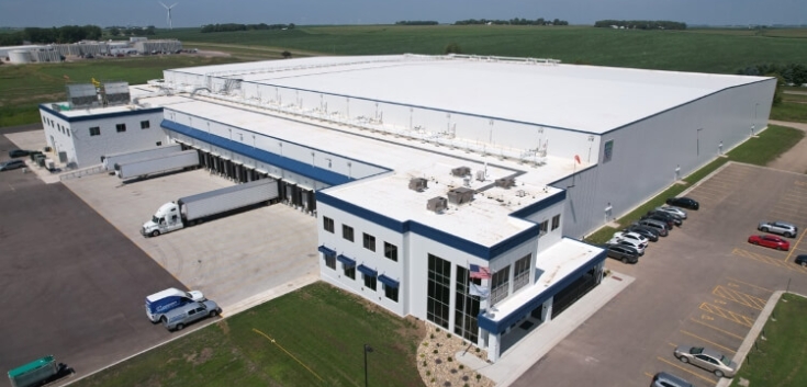 Aerial view of Lineage's Luverne cold storage warehouse in Minnesota, featuring a modern facility with multiple loading docks, parked trucks, and surrounding farmland for efficient cold chain operations.