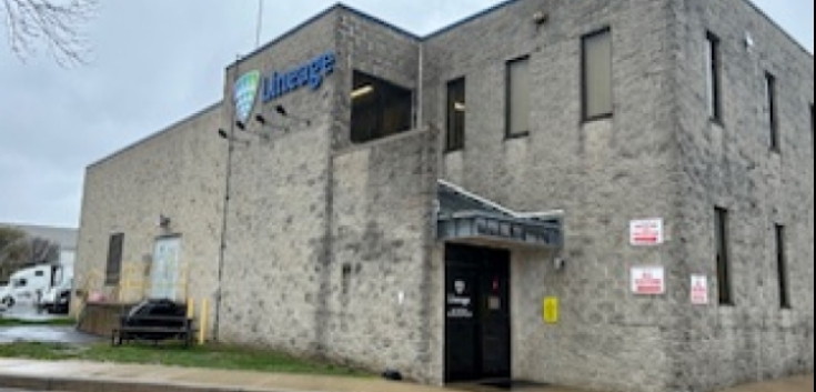 Exterior view of Lineage's New Castle cold storage warehouse in Delaware, featuring a gray stone building with company signage and secure entry, supporting cold chain logistics operations.