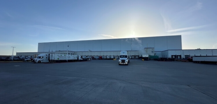 Wide view of Lineage's Pasco cold storage warehouse in Washington, with loading docks, parked trucks, and a large paved lot at sunrise, highlighting expansive logistics capacity.