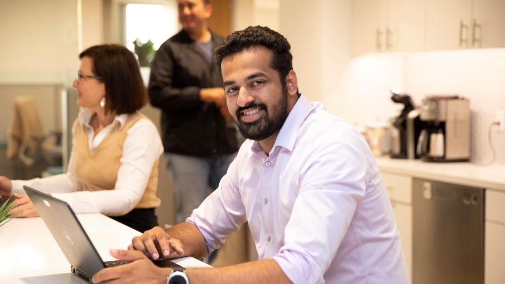 Smiling Lineage team member working on a laptop in a modern office setting, showcasing a welcoming and collaborative work environment at Lineage's Global HQ in Novi, Michigan.