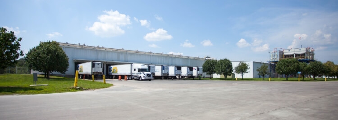 Side view of Lineage’s Unadilla cold storage facility near Atlanta, Georgia, showcasing docked refrigerated trailers, surrounding greenery, and open parking areas under a clear blue sky.