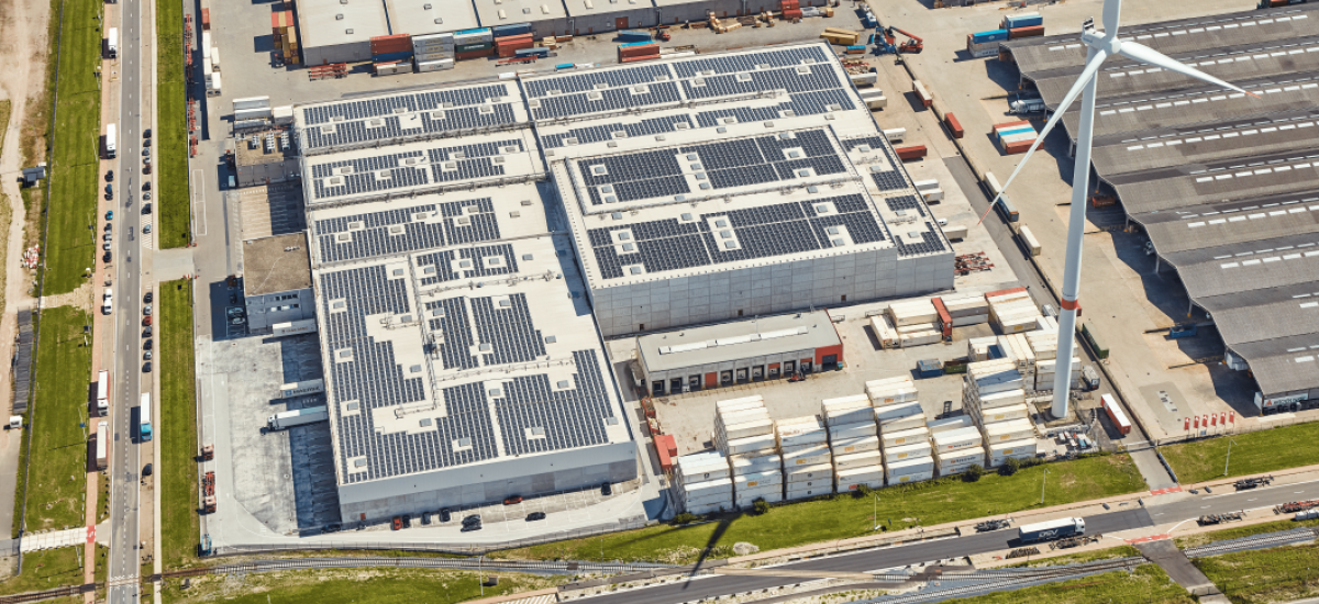 An aerial view of a cold storage facility with solar panels and wind turbine in Belgium