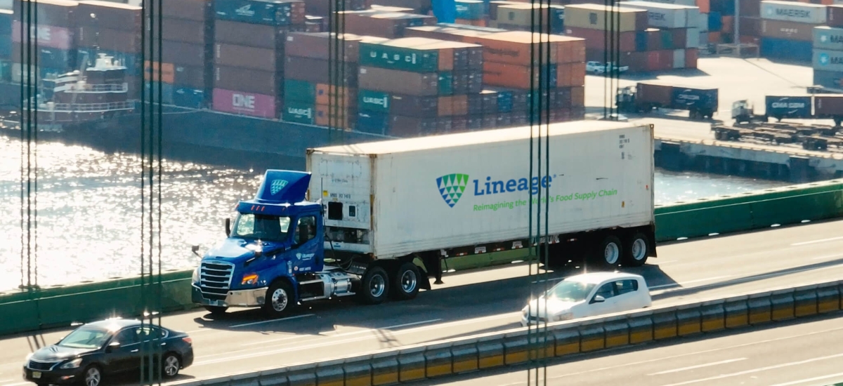 A Lineage truck crossing a bridge with a port full of shipping containers in the background, representing supply chain solutions for navigating tariffs and global trade challenges.