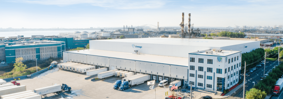 A large Lineage cold storage warehouse in New Jersey, with the Lineage logo, featuring multiple loading docks with trucks, located in an industrial area with proximity to a port.