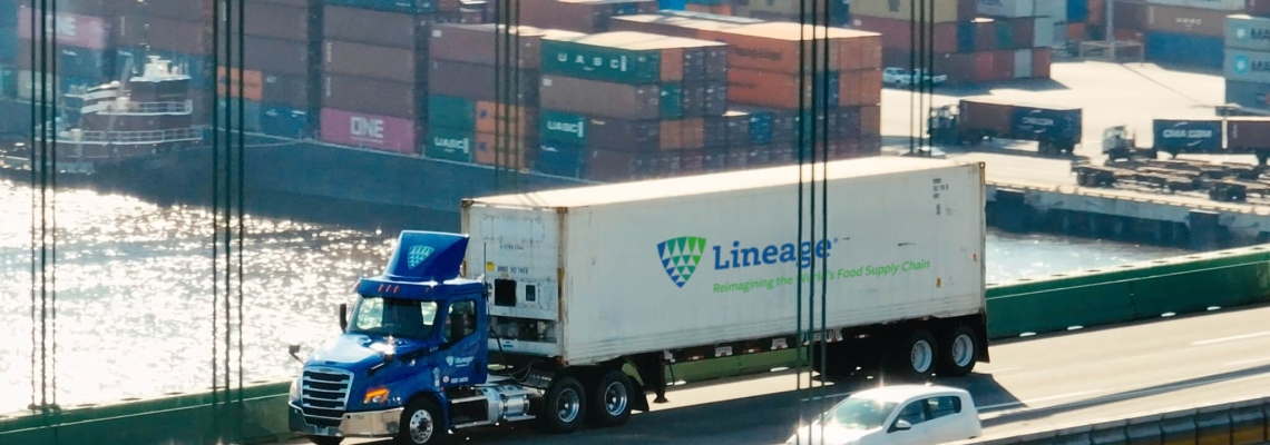 A Lineage truck crossing a bridge with a port full of shipping containers in the background, representing supply chain solutions for navigating tariffs and global trade challenges.