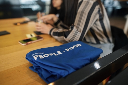 A blue shirt with white text that reads "Connecting People to Food" is folded on a table