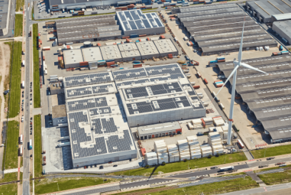 An aerial photograph of a cold storage warehouse with solar panels on its roof and wind turbine in the foreground