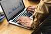 Person typing on laptop, with spreadsheets showing on screen.