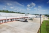 A view of Lineage's cold storage warehouse in Attalla, Alabama, showcasing multiple loading docks with semi-trucks parked for deliveries. The large white facility is surrounded by an expansive concrete lot and green landscaping under a bright blue sky with scattered clouds.